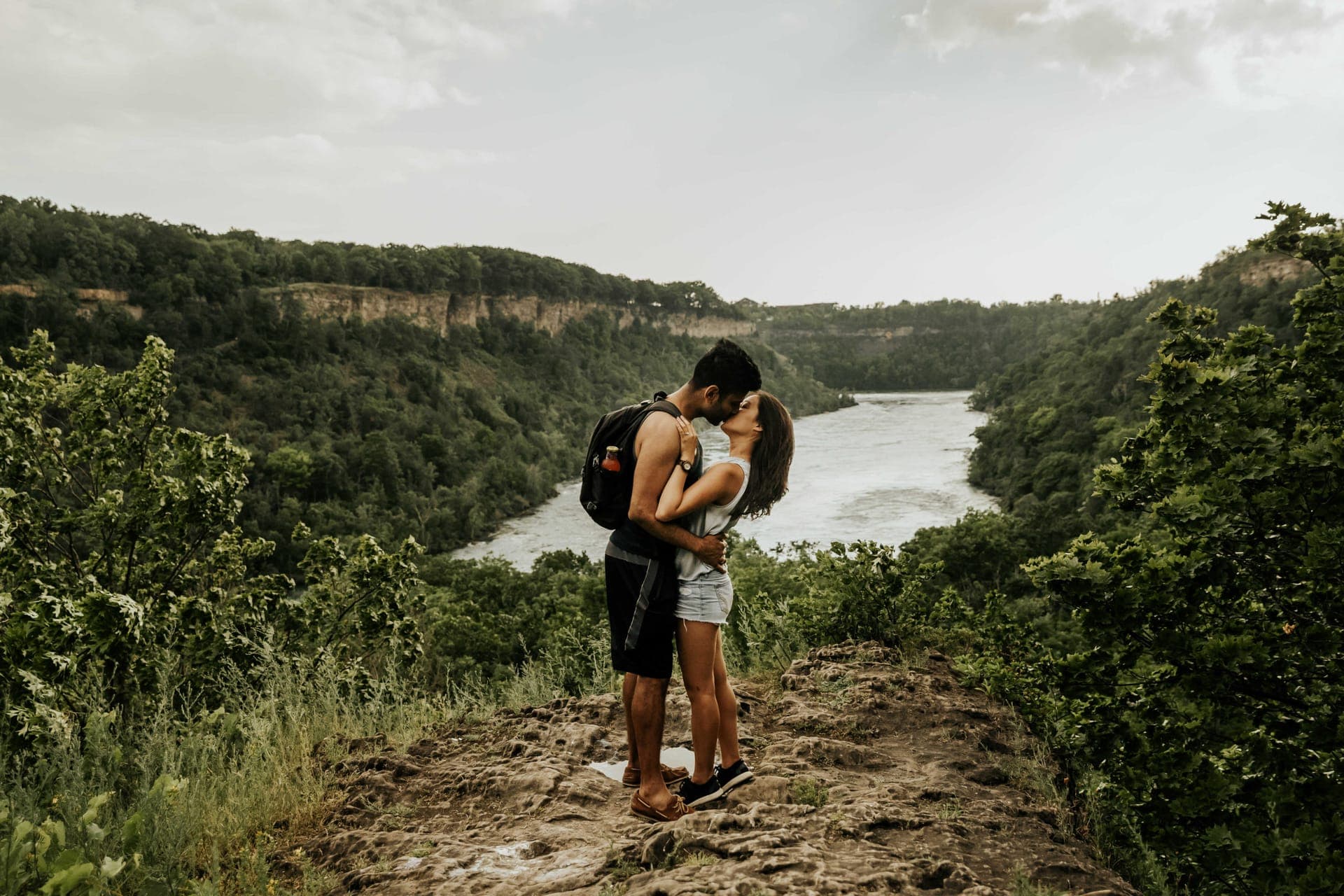 Amir and Samantha embracing on a cliff path above a river gorge